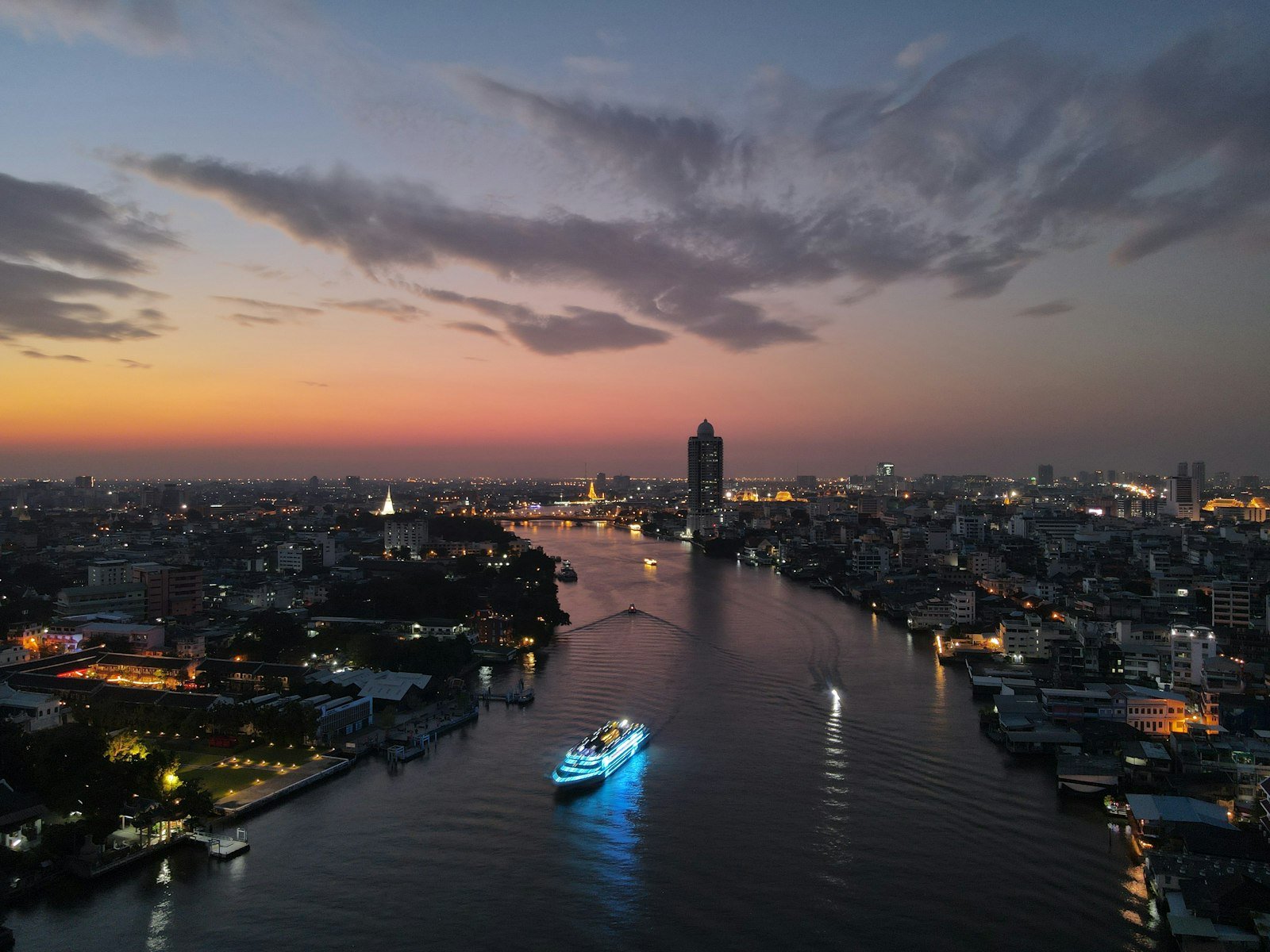 Un battello illuminato naviga sul fiume Chao Phraya a Bangkok al crepuscolo, con i grattacieli della città sullo sfondo