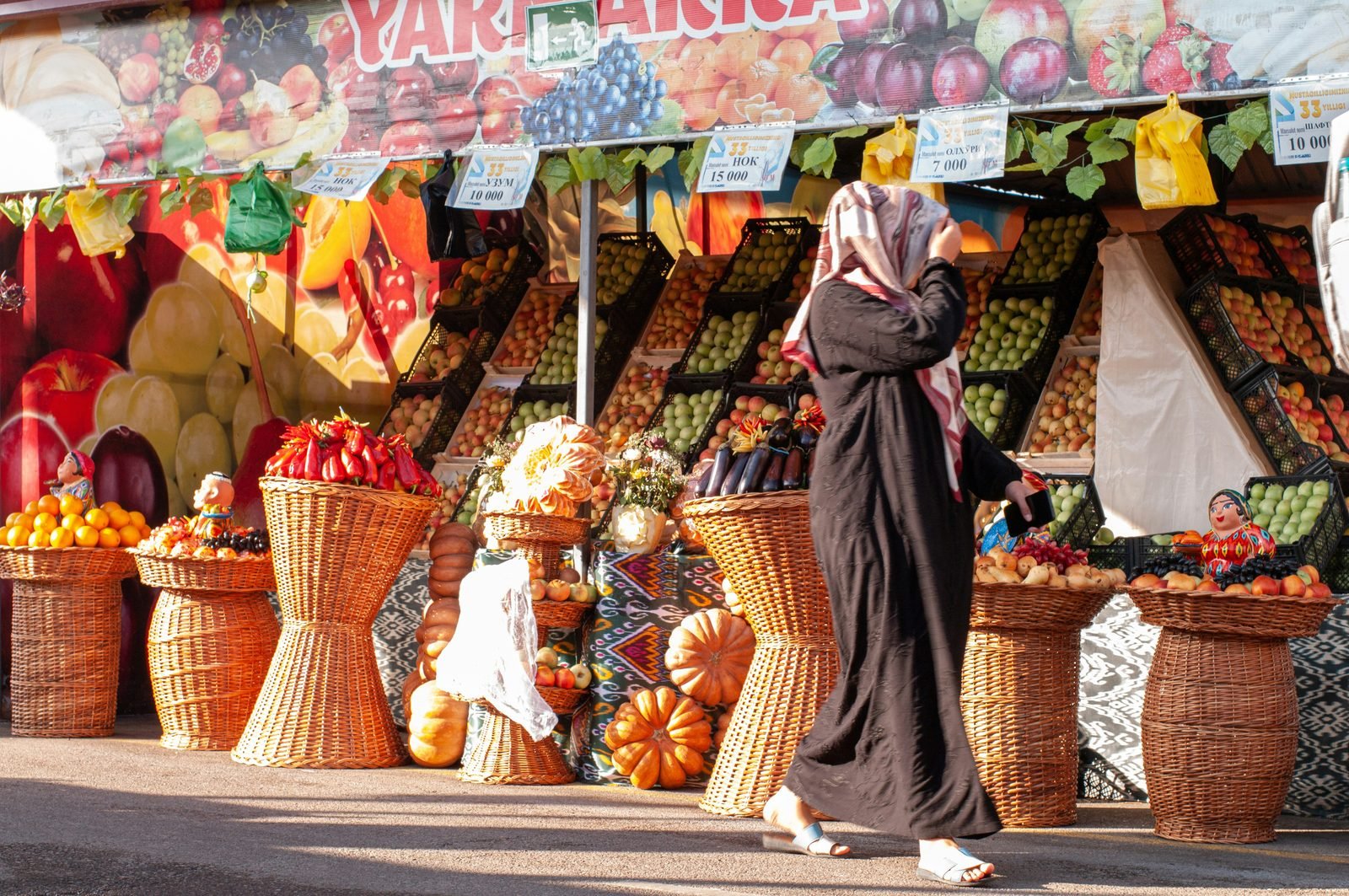 Banco di frutta e verdura al bazar Chorsu di Tashkent, con ceste di vimini, zucche e cartellini dei prezzi in som