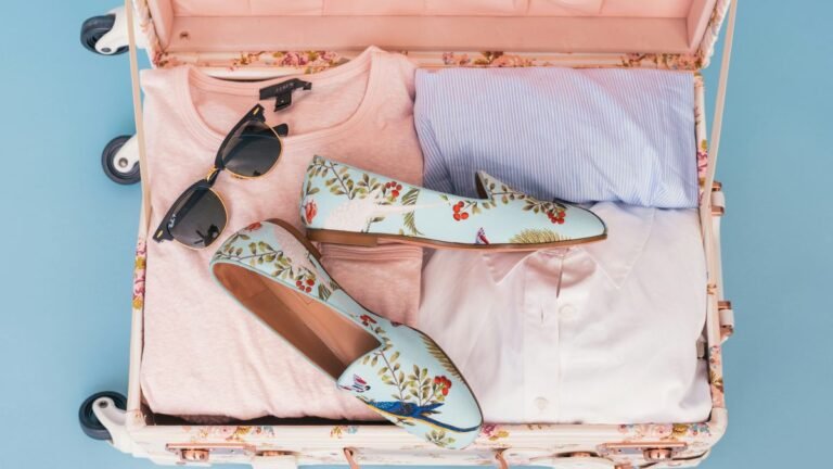 Valigia aperta con vestiti piegati, scarpe e occhiali da sole pronta per il viaggio