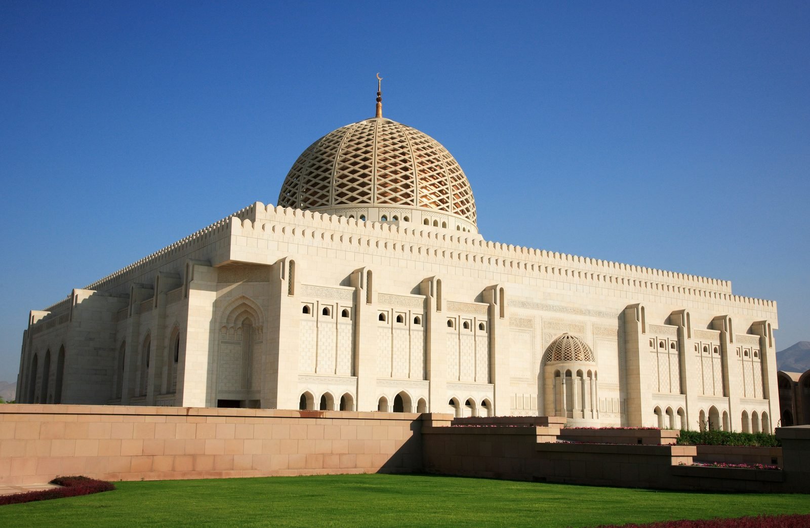 La Grande Moschea Sultan Qaboos di Muscat, in pietra chiara con la cupola traforata, sotto un cielo azzurro