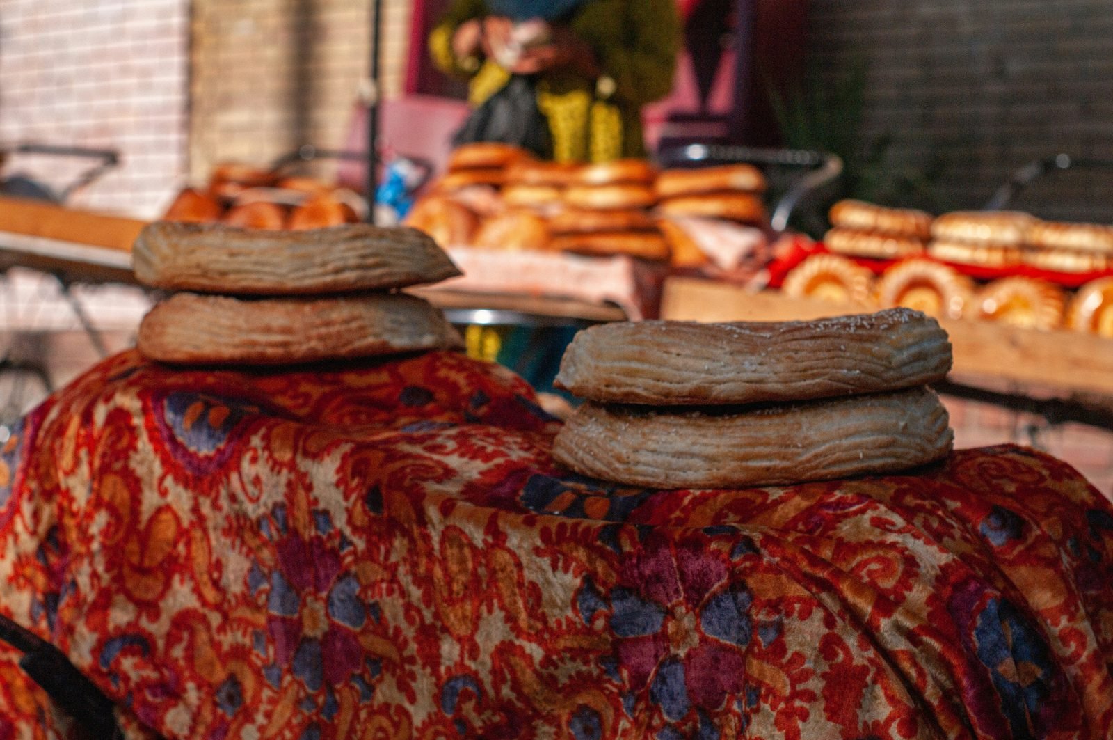 Pani uzbeki rotondi (non) impilati su un telo ricamato al banco di un bazar di Tashkent