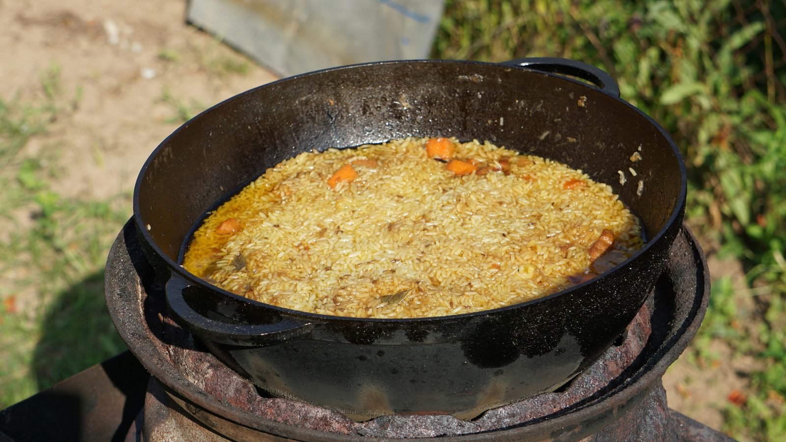 plov ricetta uzbeka Plov uzbeko: la ricetta originale passo passo Plov in cottura in un kazan di ghisa all'aperto, con il riso che affiora tra le carote